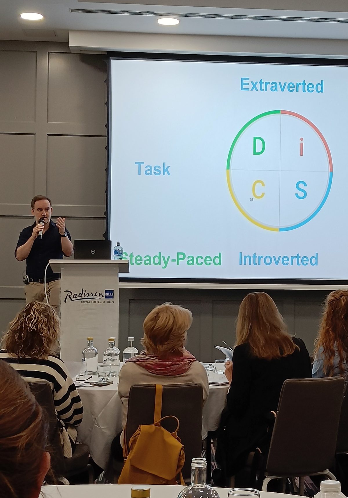 David O'Grady on stage delivering an Everything DiSC workshop, the DiSC map on the screen behind him